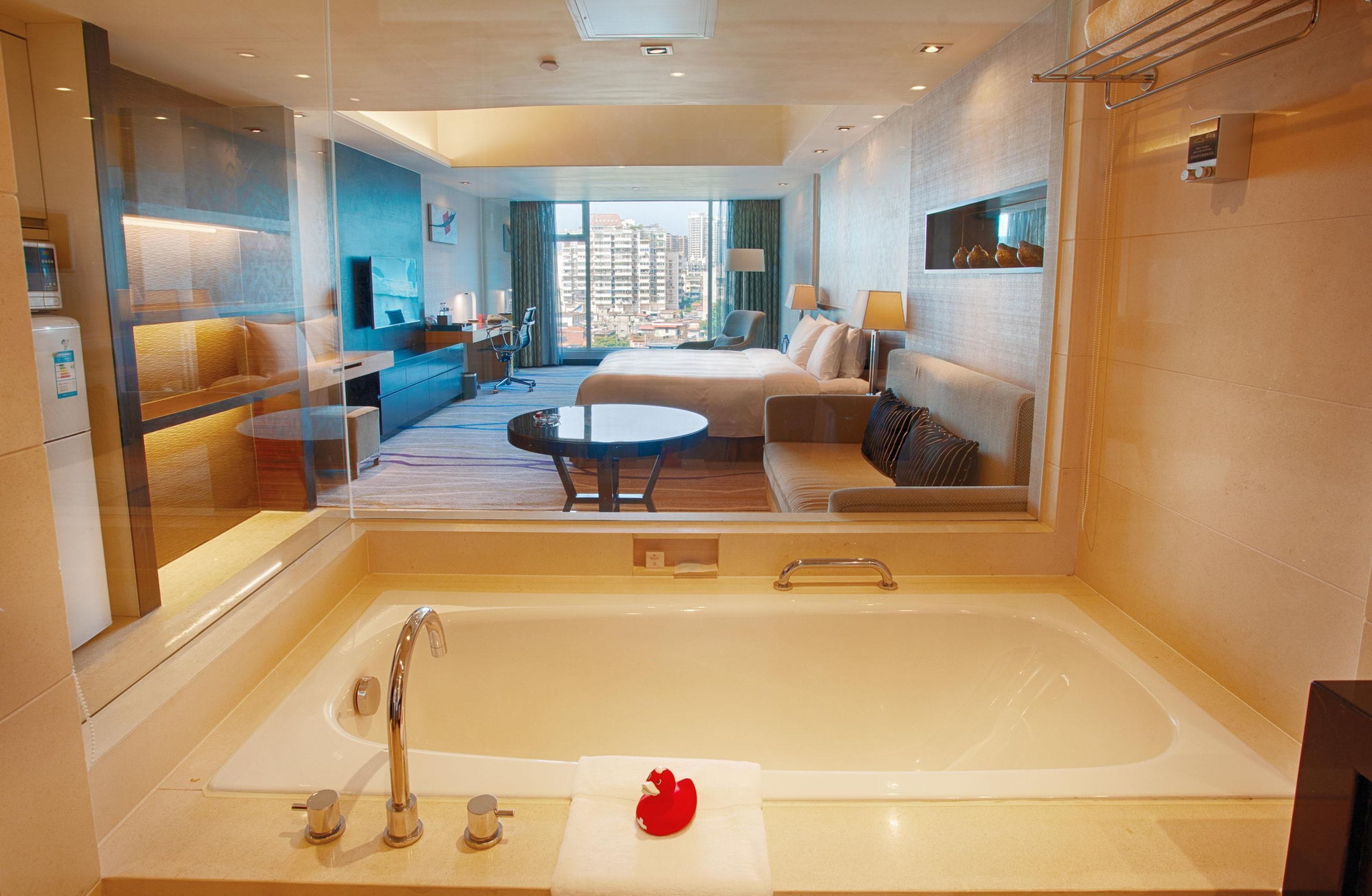 Habitación de hotel moderna con una bañera grande, un sofá, una mesa de comedor y vistas a la ciudad.