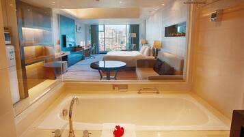 Habitación de hotel moderna con una bañera grande, un sofá, una mesa de comedor y vistas a la ciudad.