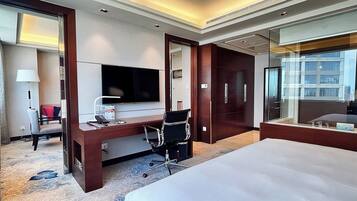 A hotel room with a large bed, a desk with a computer, a television, and a wardrobe.