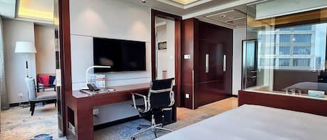 A hotel room with a large bed, a desk with a computer, a television, and a wardrobe.