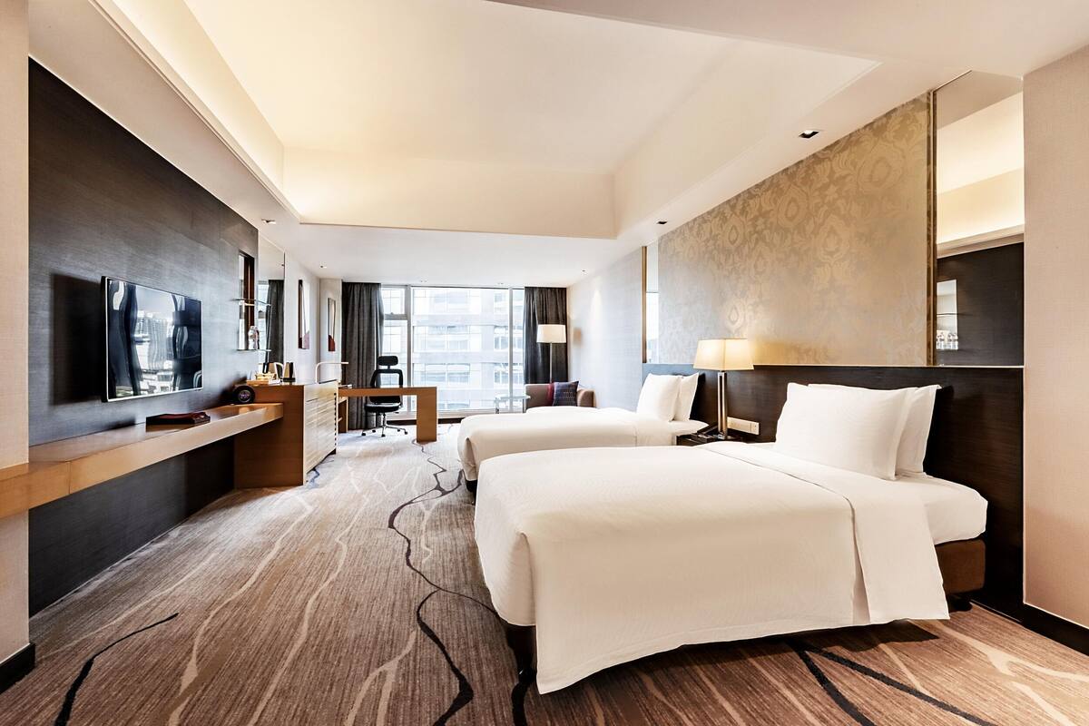Une chambre d’hôtel avec deux lits, une télévision, un bureau et une grande fenêtre.