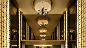 Un hall d’entrée spacieux, agrémenté d’un imposant lustre, d’un motif décoratif sur le sol et d’un grand emblème circulaire.