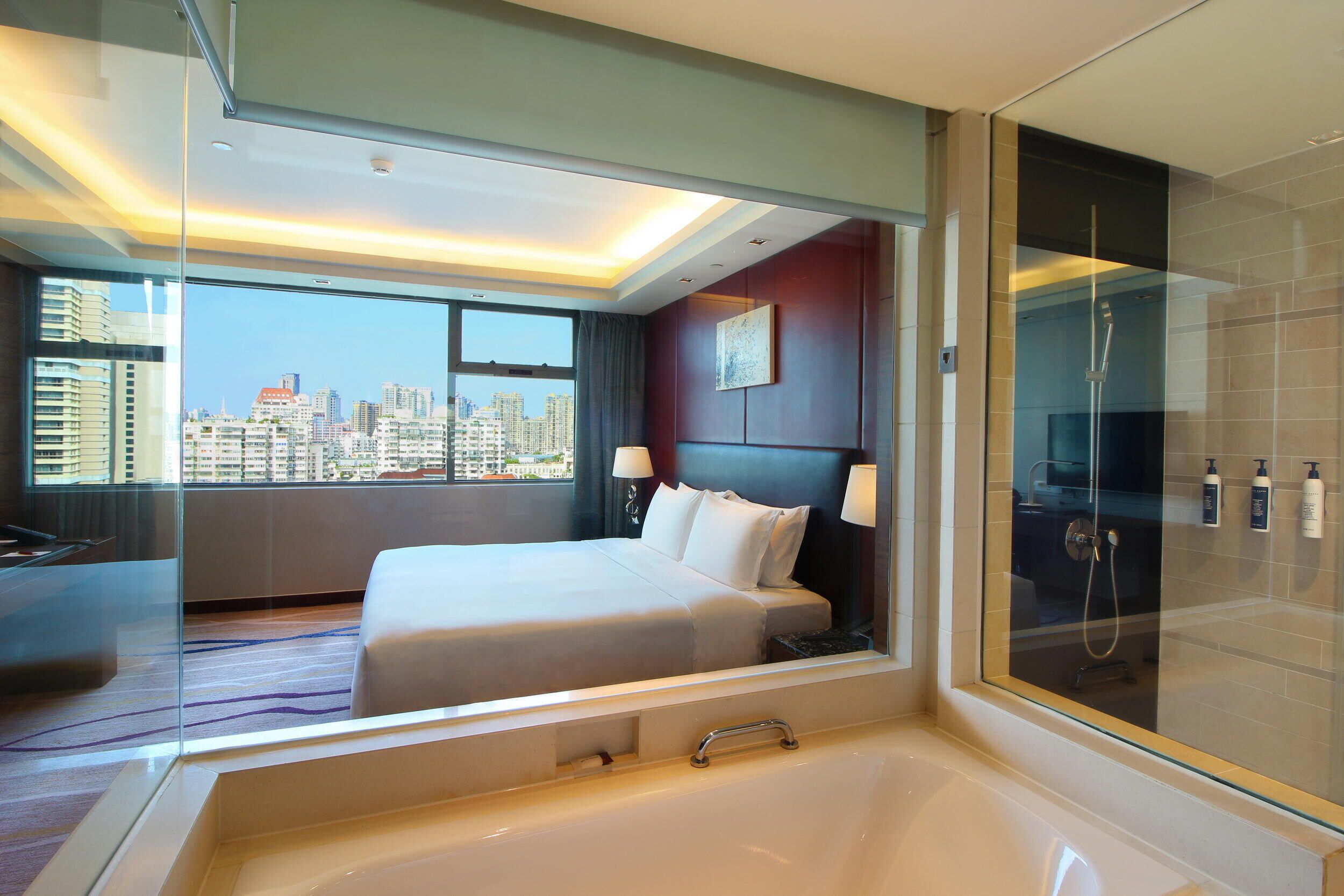 Ein modernes Hotelzimmer mit einem großen Bett, einer Duschkabine aus Glas und Blick auf die Stadt.