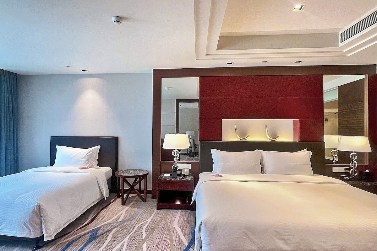 Une chambre d’hôtel avec deux lits, une petite table, un miroir et une table de chevet avec des lampes.