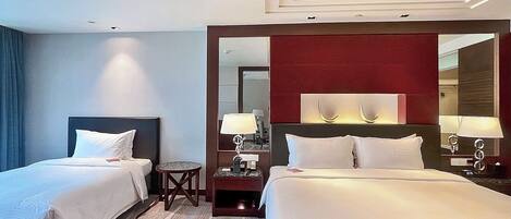 Habitación de hotel con dos camas, una mesita, un espejo y una mesita de noche con lámparas.