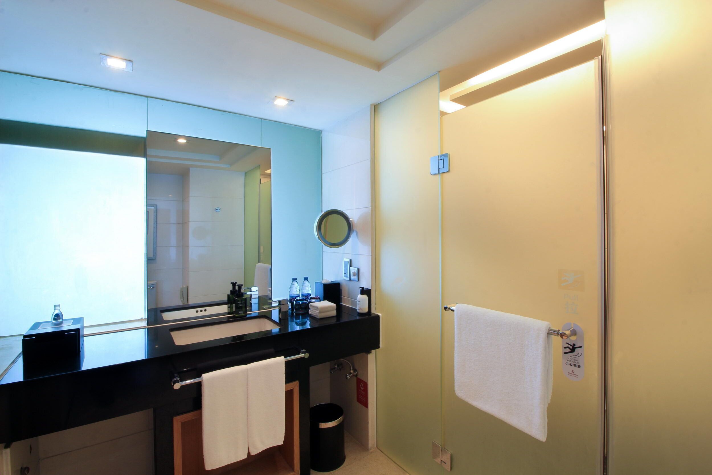 A modern bathroom with a black sink, a large mirror, and a glass shower door.