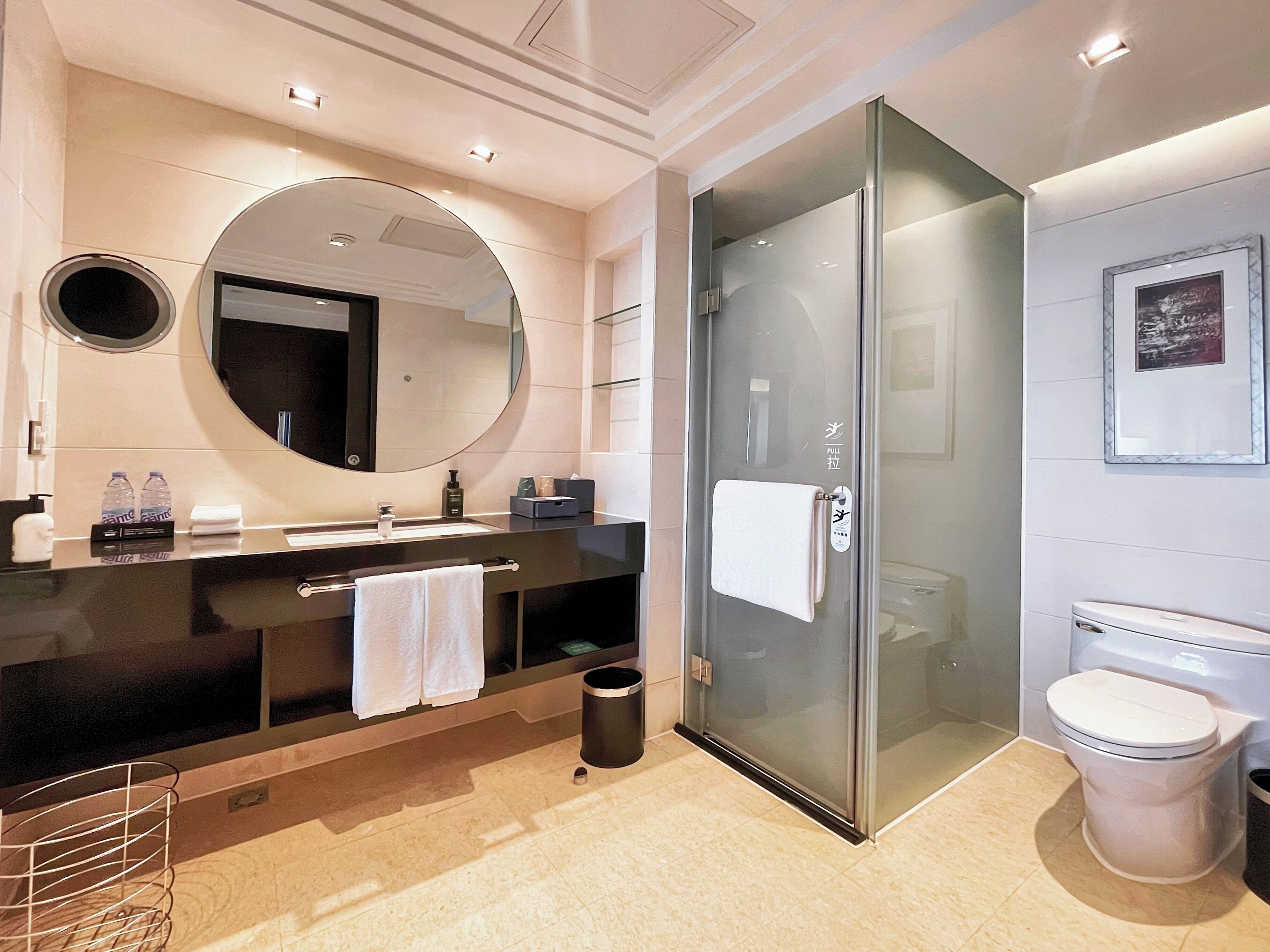 Un baño moderno con ducha envuelta en vidrio, un espejo grande y un mueble de tocador negro con toallero.