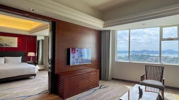 A hotel room with a bed, a TV mounted on the wall, a wooden cabinet, a chair, and a large window offering a city view.