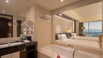 A hotel room with a large mirror, a bathtub, a double bed, and a view of the city.