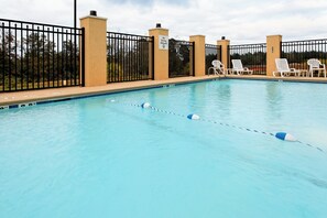 A swimming pool with a black metal fence, white lounge chairs, and a clear sky.