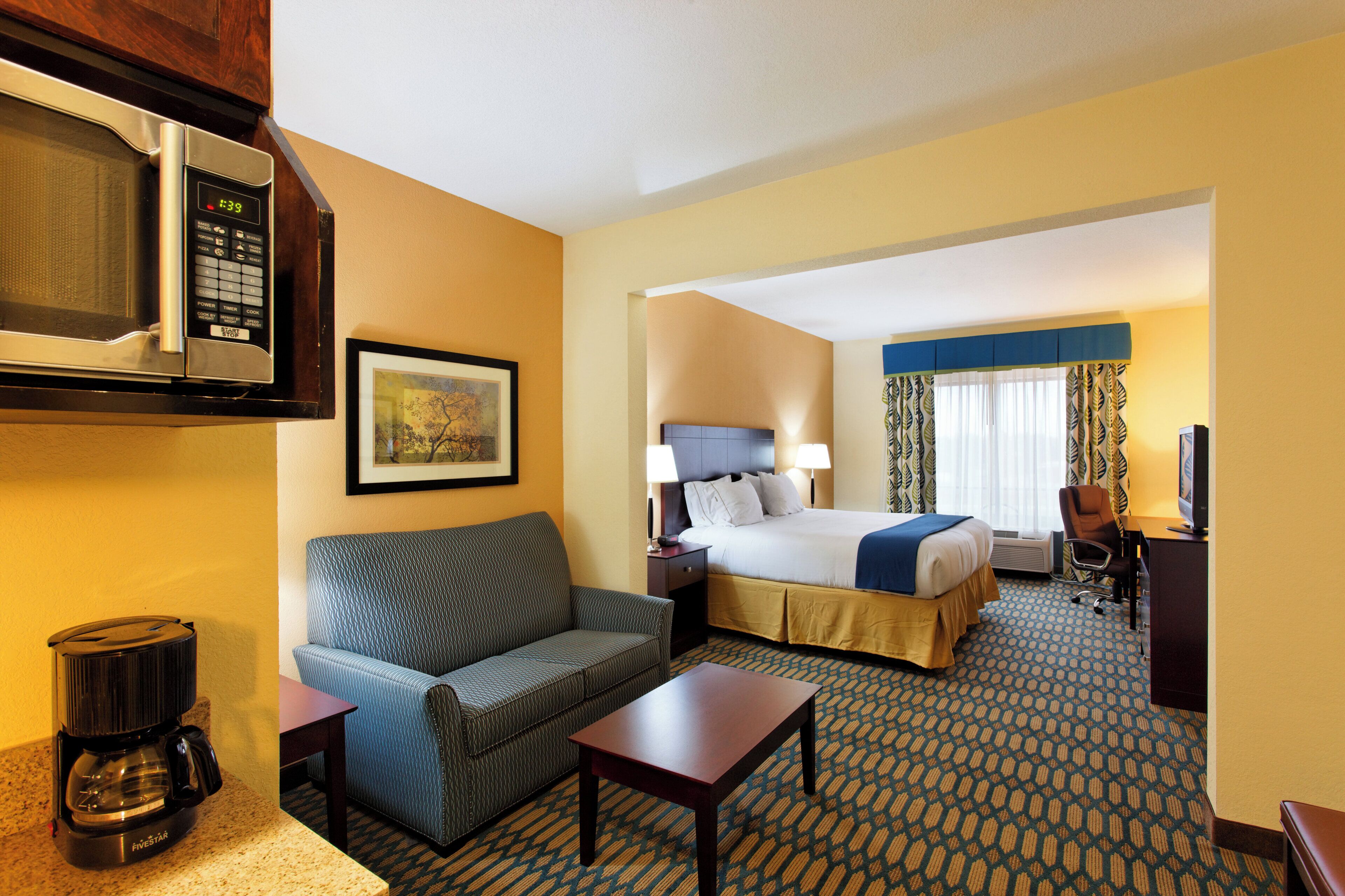 A hotel room with a bed, a sofa, a coffee maker, a TV, and a framed picture on the wall.