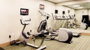 Un gimnasio equipado con cintas de correr, elípticas y un espejo grande.