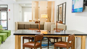 A modern hotel room with a dining area, a sofa, and a TV mounted on the wall.