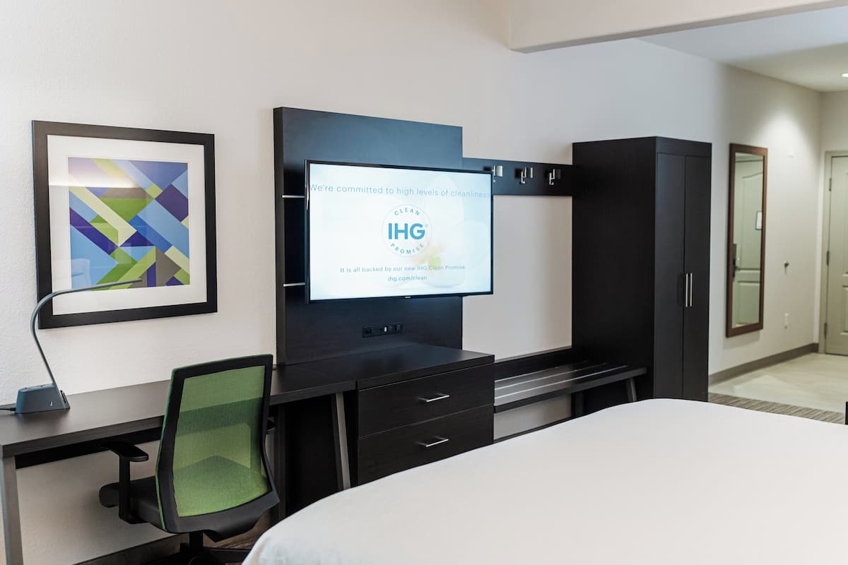 A hotel room with a bed, a desk with a chair, a TV mounted on the wall, and a wardrobe.