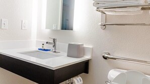 A bathroom with a white sink, a mirror, a towel rack with folded towels, and a toilet paper holder.
