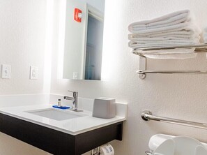 A bathroom with a white sink, a mirror, a towel rack with folded towels, and a toilet paper holder.