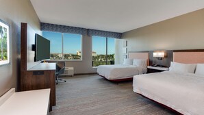 Habitación de hotel con dos camas, un escritorio, una silla, un televisor y vistas de la ciudad.