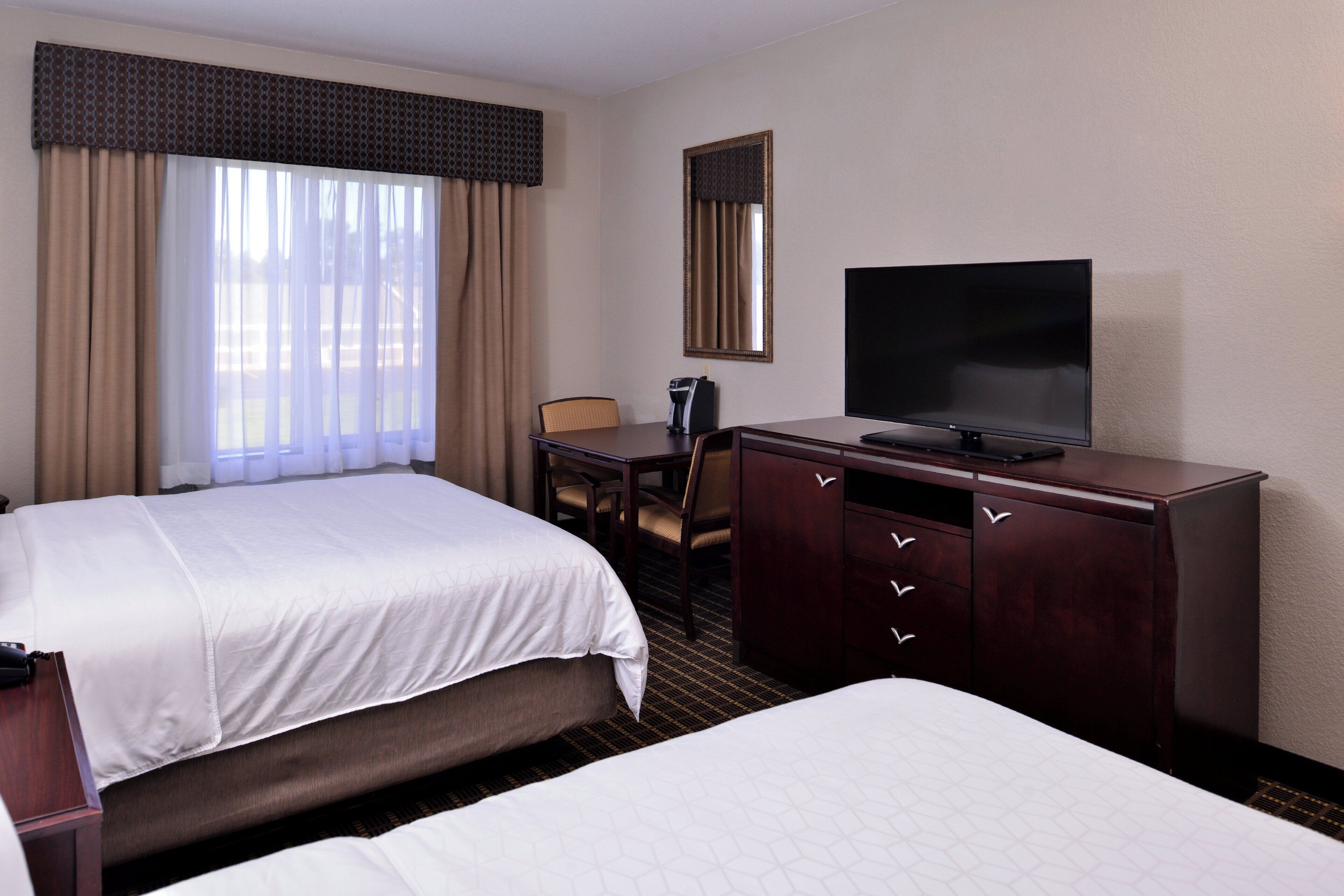 A hotel room with two beds, a desk, a television, and a mirror.
