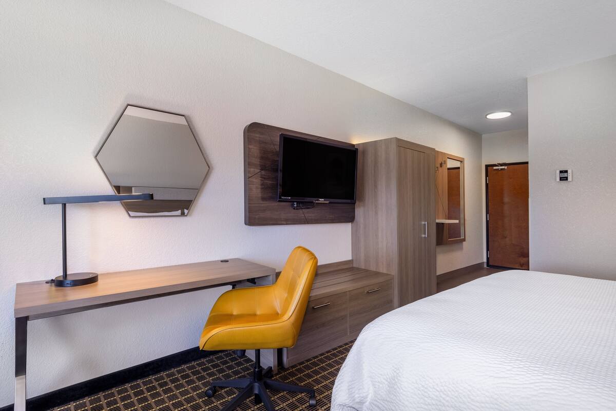 A hotel room with a bed, a desk, a chair, a TV mounted on the wall, and a wardrobe.