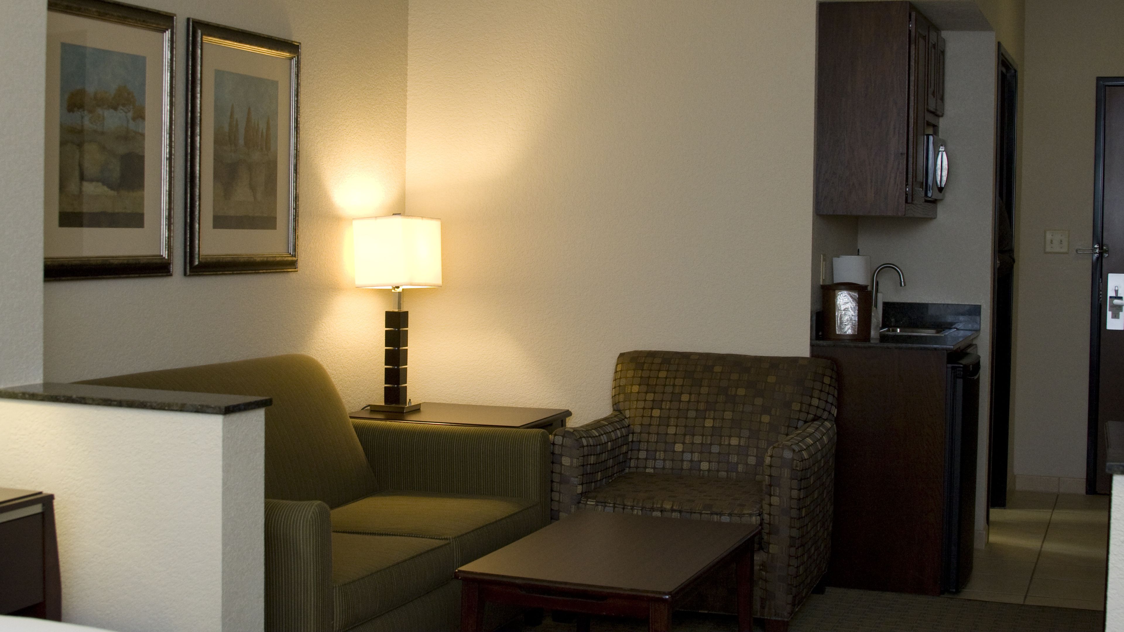 A compact living space with a sofa, a small table, a lamp, and a kitchenette area.