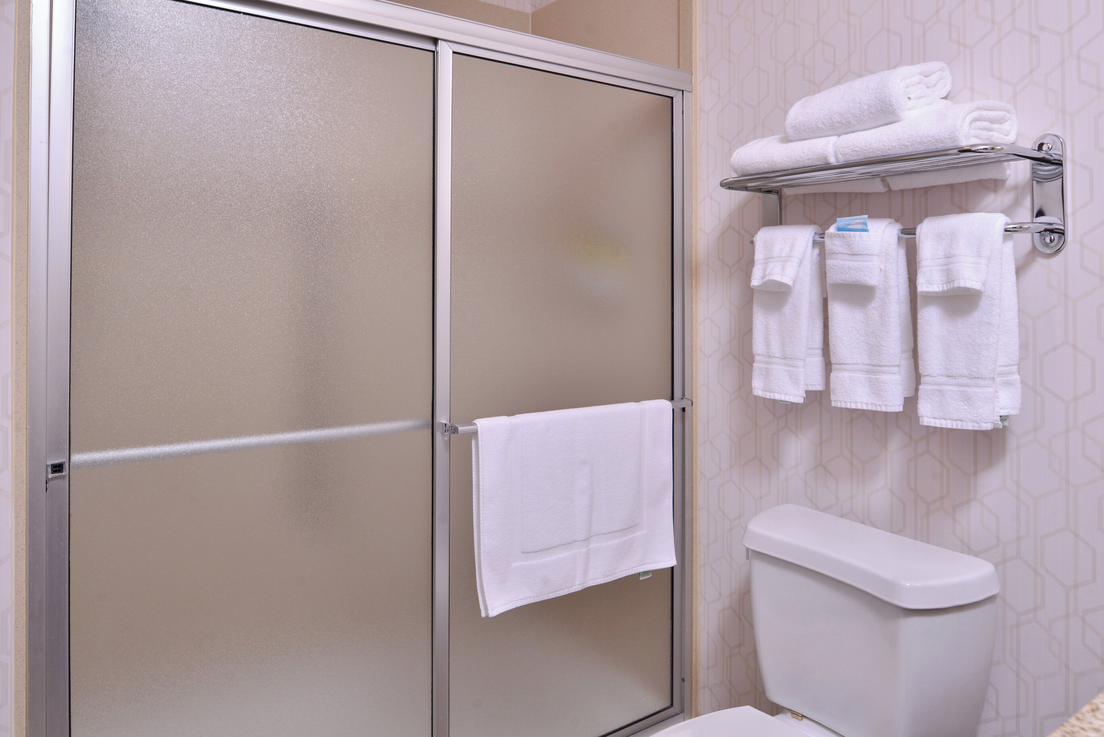 Un baño con cabina de ducha, inodoro y un perchero con toallas.