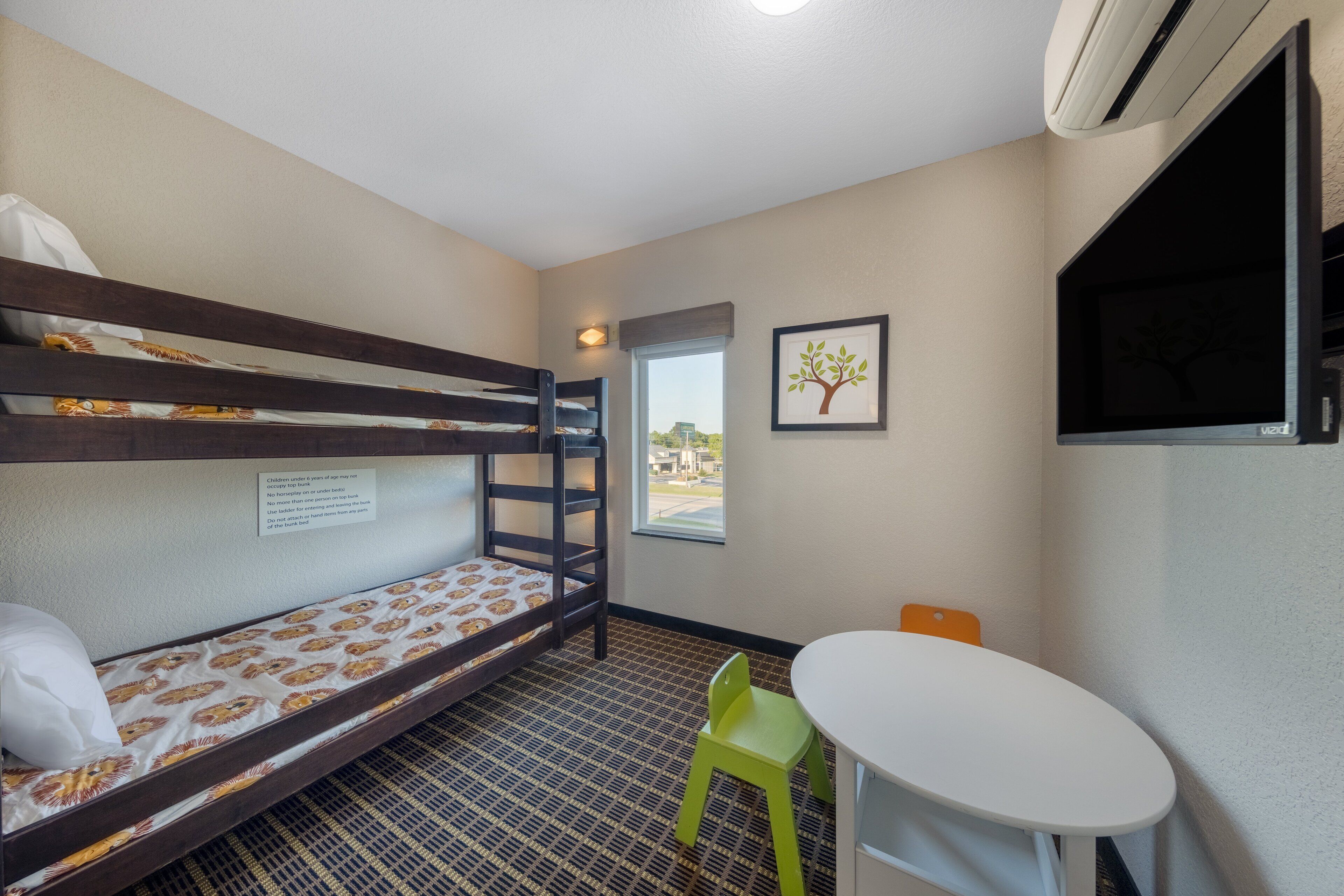 A bunk bed with a note, a small table, a green chair, and a window with a view.