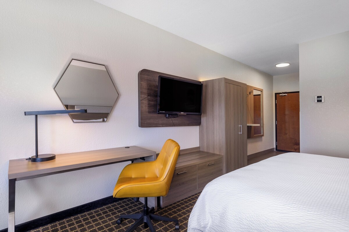 A hotel room with a bed, a desk, a chair, a TV mounted on the wall, and a wardrobe.
