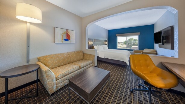 Habitación de hotel con sofá, cama, escritorio, silla, lámpara y un cuadro.