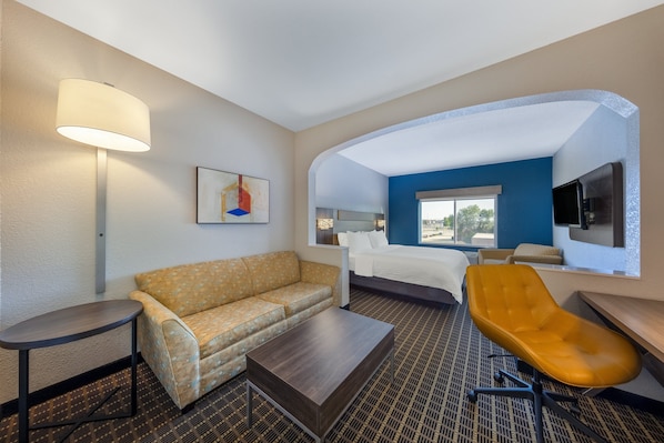 A hotel room with a sofa, a bed, a desk, a chair, a lamp, and a painting.
