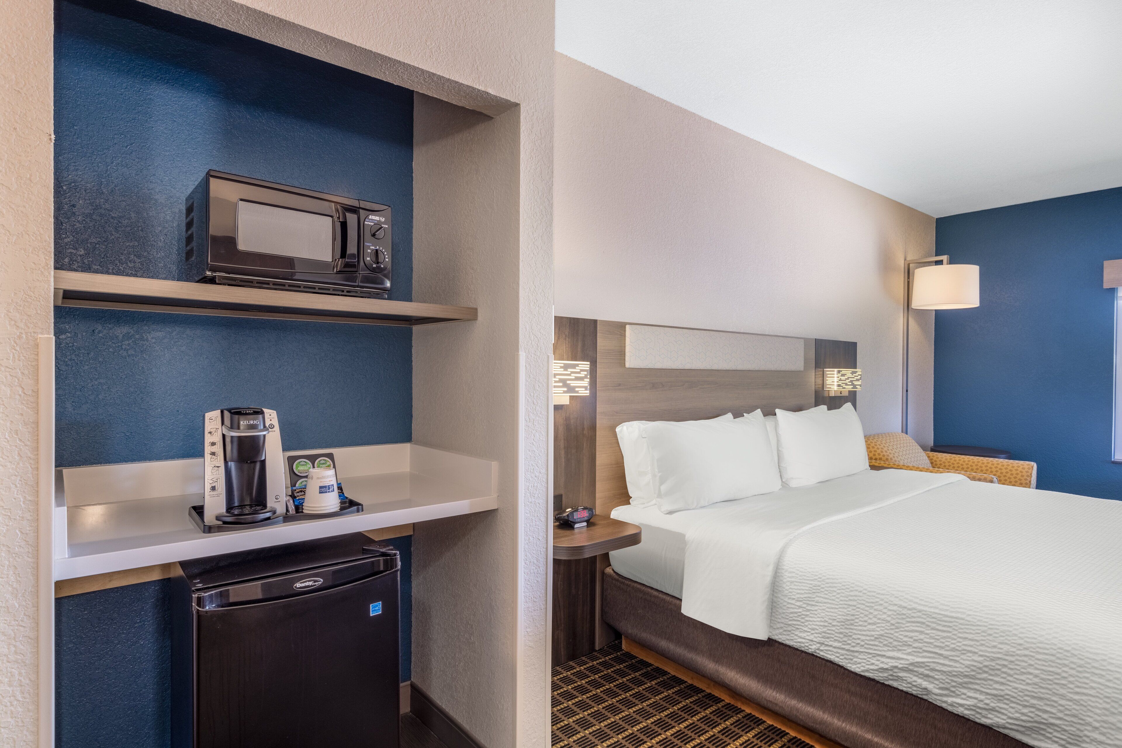 A hotel room with a bed, a coffee maker, a microwave, and a mini-fridge.