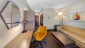 Una habitación de hotel moderna con un escritorio de madera, un sillón amarillo, un sofá, un espejo grande y un cuadro en la pared.