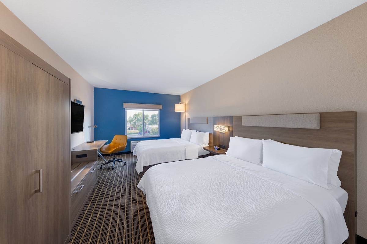 A hotel room with two beds, a desk, a chair, and a TV.