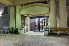 L’entrée d’un hôtel, avec une façade en briques, une porte d’entrée en verre et un espace pavé aménagé avec des sièges.
