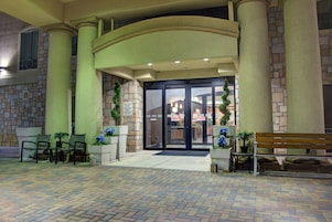 Fachada de hotel de ladrillo, puerta de entrada de vidrio y zona pavimentada con asientos.