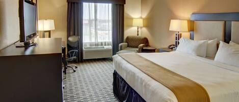 A hotel room with a large bed, a desk with a computer, a chair, a TV, and a window with curtains.