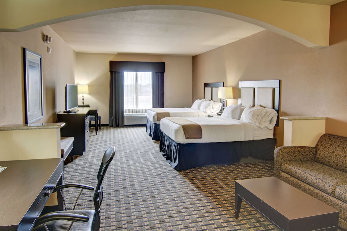 Ein Hotelzimmer mit einem Bett, zwei Nachttischen, einem Schreibtisch, einem Sessel und einem gemusterten Teppich.