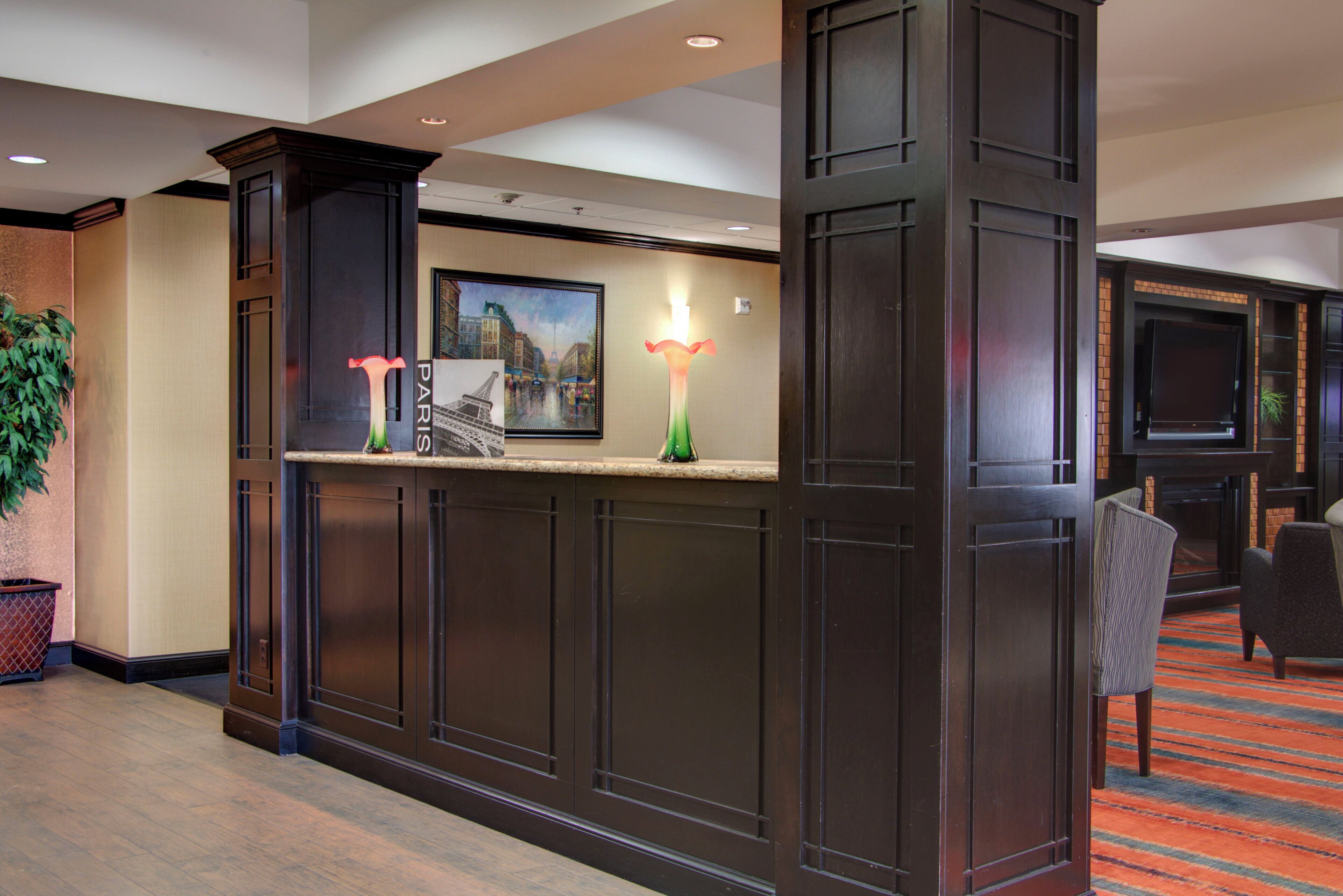 A reception area with a dark wood reception desk, a framed cityscape painting, and a potted plant.