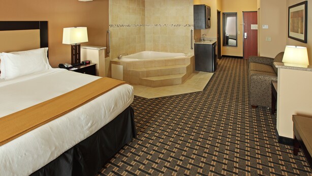 A hotel room with a large bed, a separate bathroom with a bathtub, a desk with a chair, and a patterned carpet.