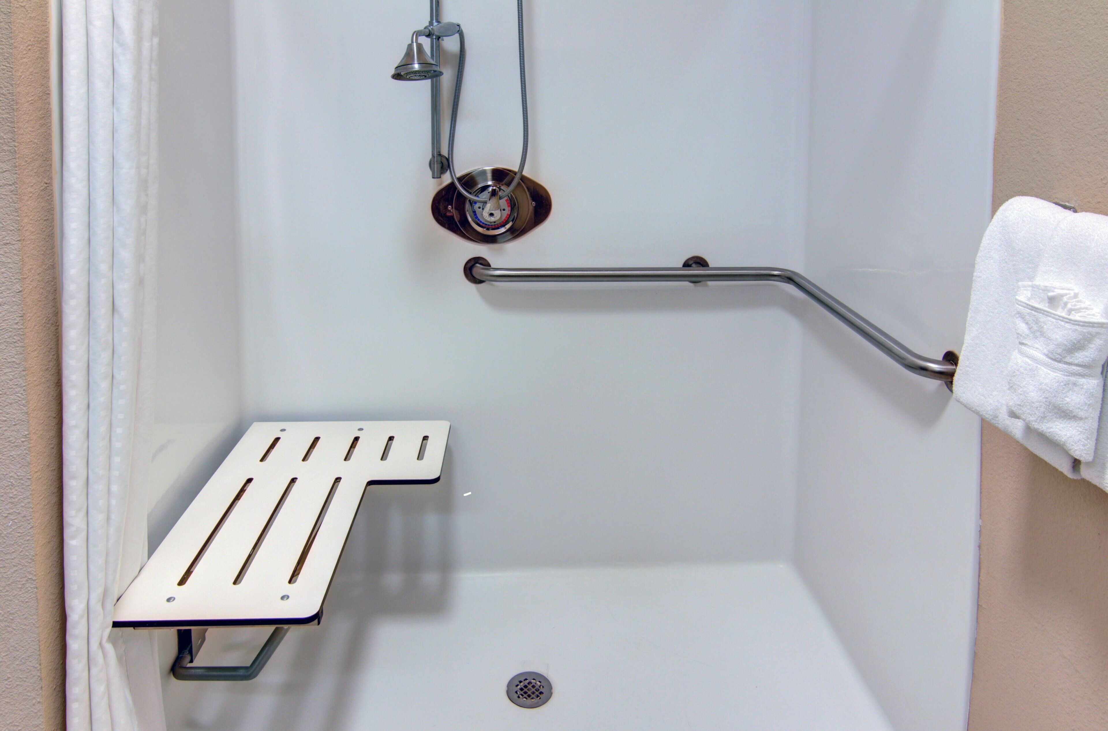 A shower with a grab bar, a white towel, and a metal shower seat.