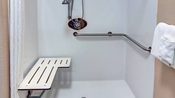 A shower with a grab bar, a white towel, and a metal shower seat.