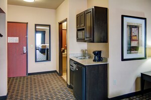 Habitación de hotel con kitchenette, una puerta que da al baño y un cuadro en la pared.