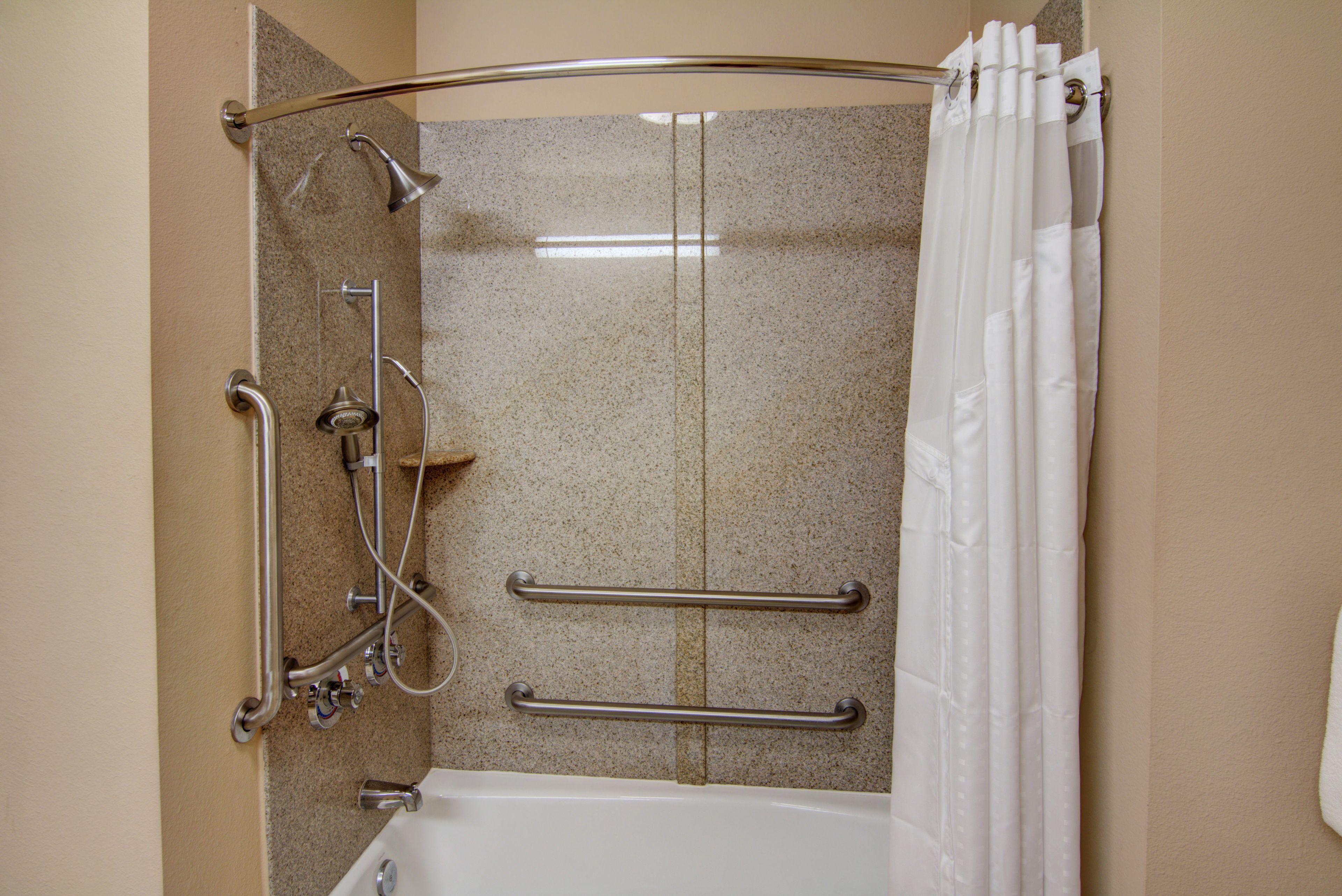 Baño con ducha, barras de apoyo y bañera.