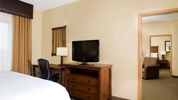 A hotel room with a bed, a desk with a television, a chair, and a dresser.