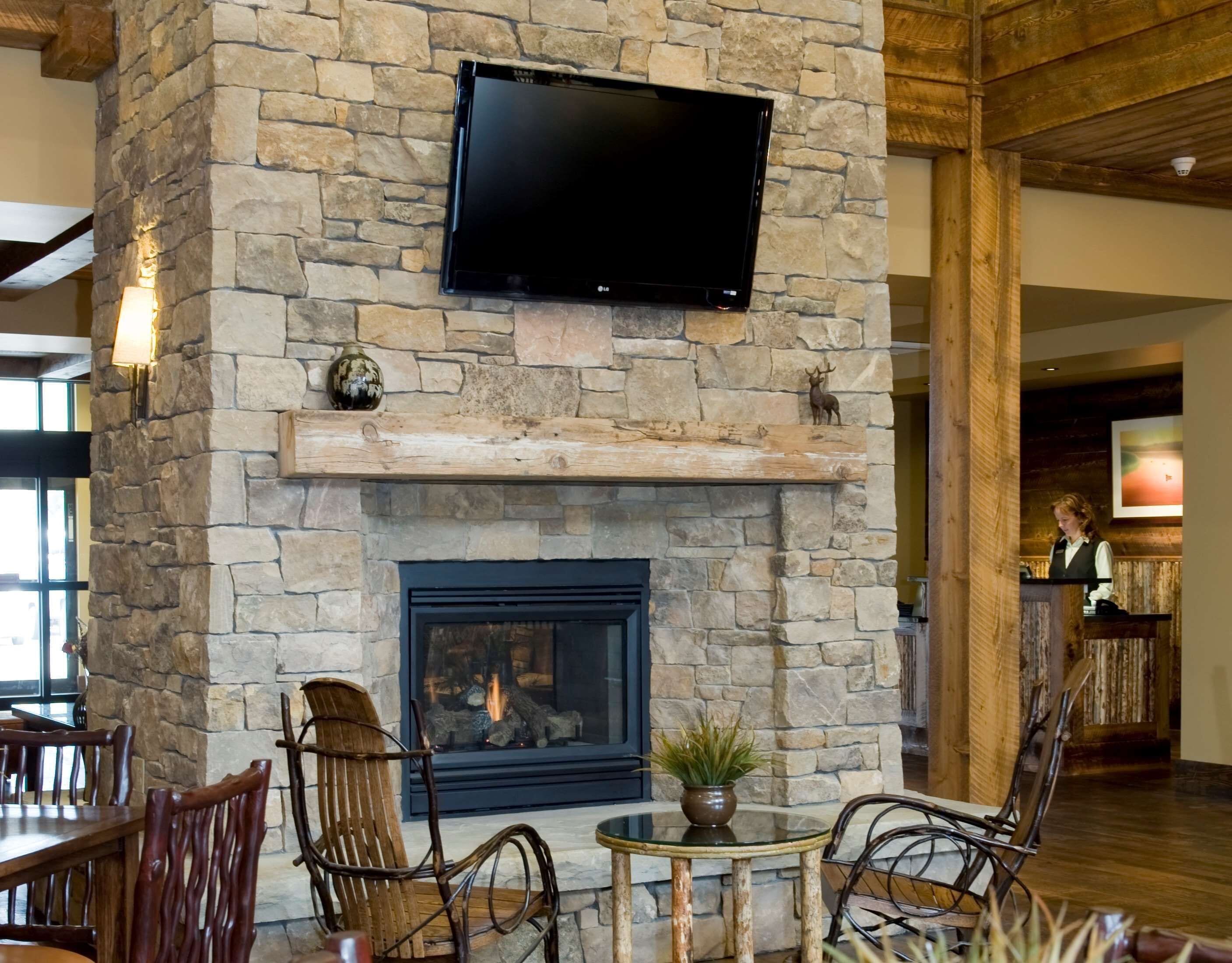 A stone fireplace with a TV mounted above it, surrounded by wooden chairs and a small table with a plant.