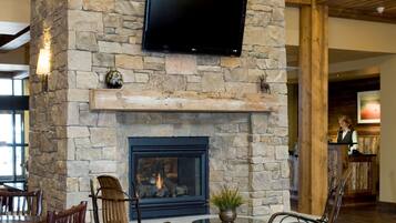 A stone fireplace with a TV mounted above it, surrounded by wooden chairs and a small table with a plant.