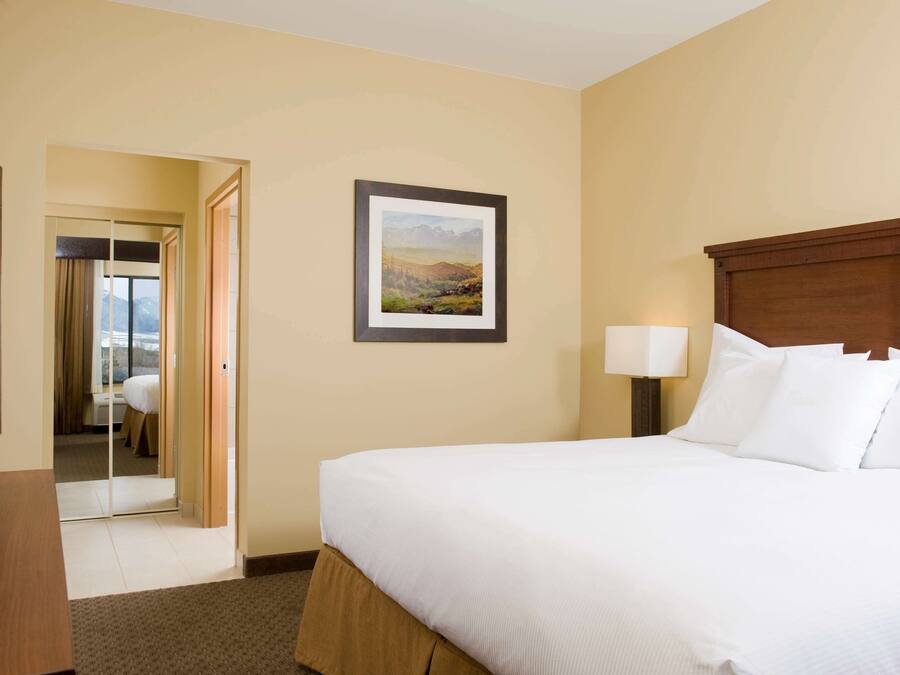 A hotel room with a bed, a television, a framed picture on the wall, and a door leading to another room.