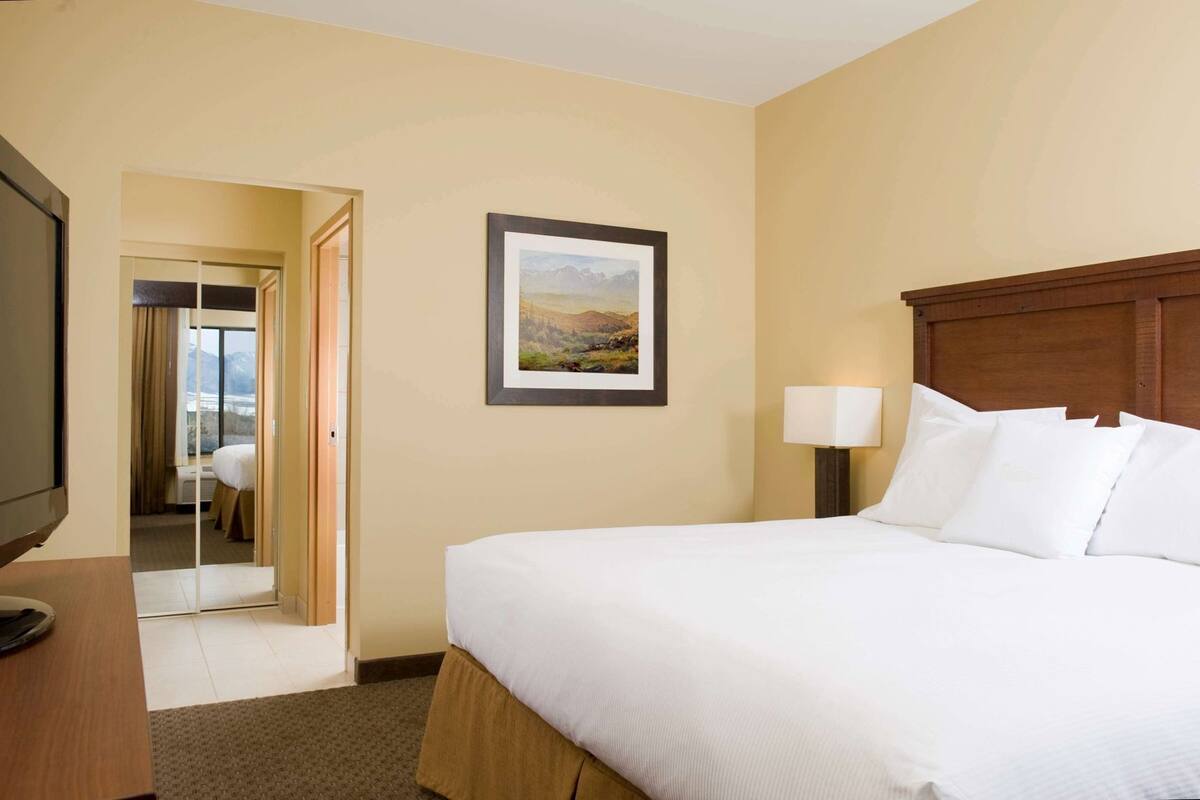 A hotel room with a bed, a TV, a framed picture, and a lamp.