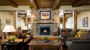 A cozy living room with a stone fireplace, leather sofas, and wooden beams on the ceiling. - Homewood Suites by Hilton Bozeman (Bozeman)