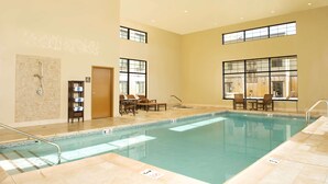 An indoor swimming pool with clear water, surrounded by beige walls and large windows. - Homewood Suites by Hilton Bozeman (Bozeman)