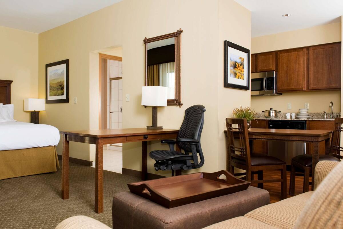 A hotel room with a bed, desk, office chair, dining table, and kitchenette.